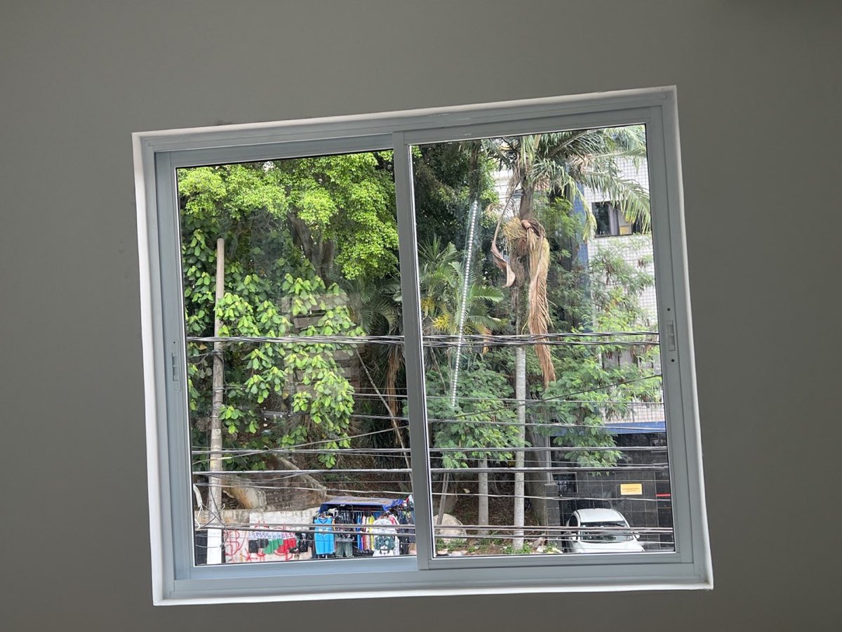 Janela ampla de alumínio branco com grade de proteção e vista para a rua. Obra da VitraAlu em Pirituba, São Paulo.