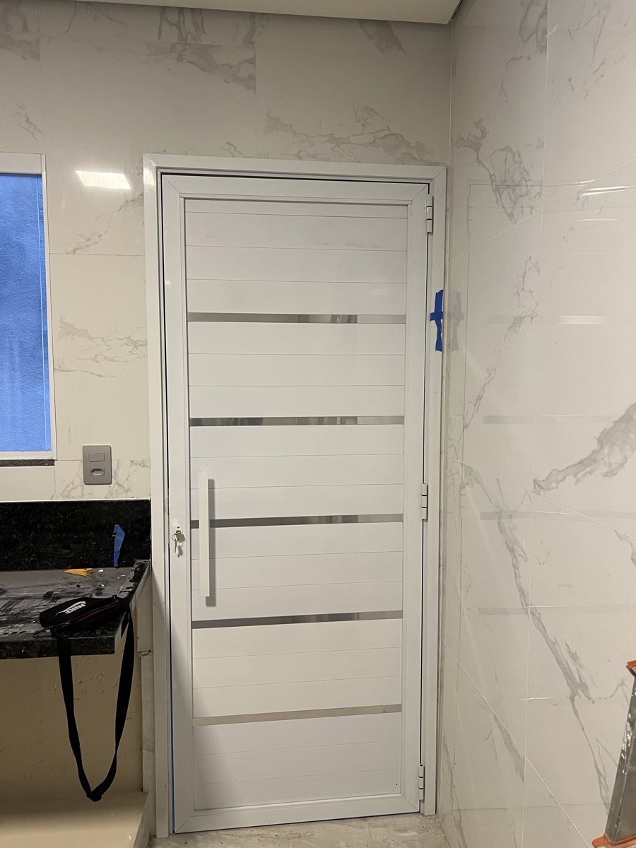Porta de alumínio branco com frisos horizontais em aço inox, instalada em ambiente revestido de mármore. Obra da VitraAlu em Vila Andrade, São Paulo.