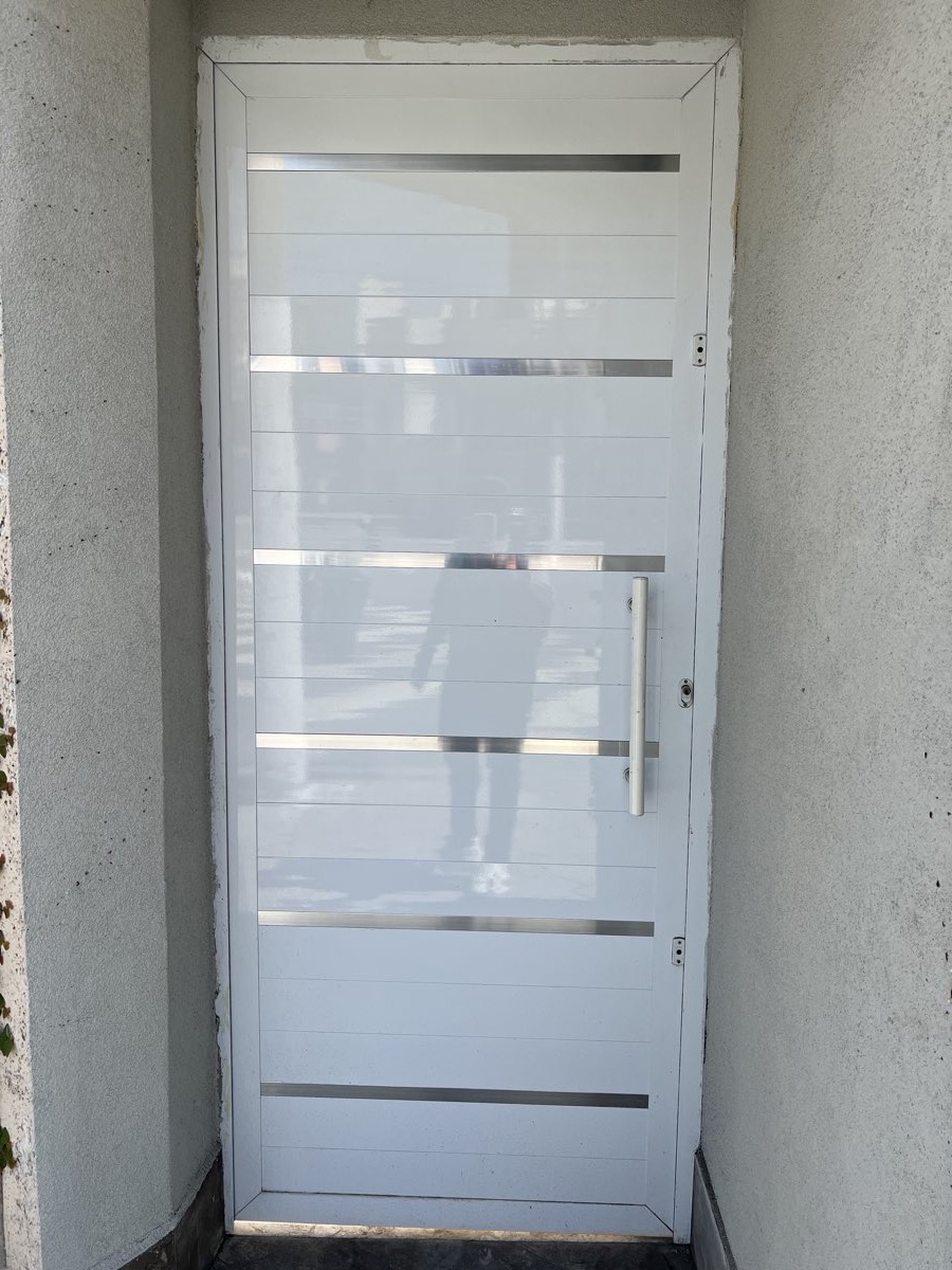 Porta de entrada em alumínio branco com frisos em aço inox e puxador tubular. Obra da VitraAlu em Vila Andrade, São Paulo.