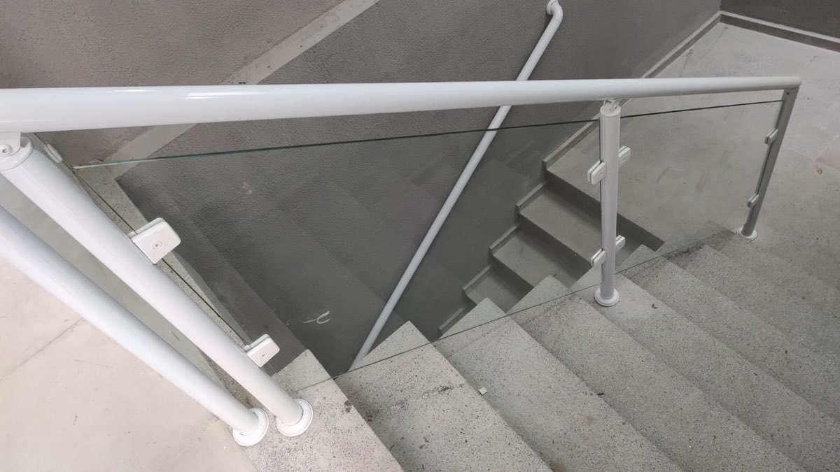 Guarda-corpo de vidro temperado com montantes e corrimão em alumínio branco, instalado em escada. Obra da VitraAlu em Consolação, São Paulo.