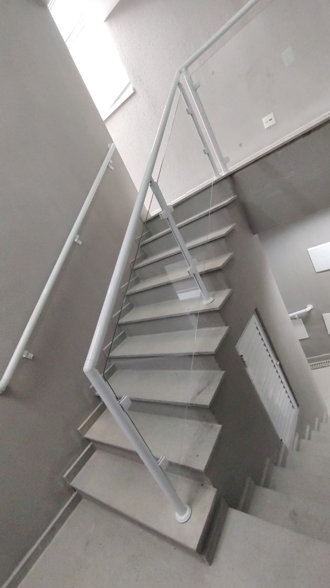 Escada com guarda-corpo de vidro temperado e corrimão em alumínio branco acompanhando os degraus. Obra da VitraAlu em Consolação, São Paulo.