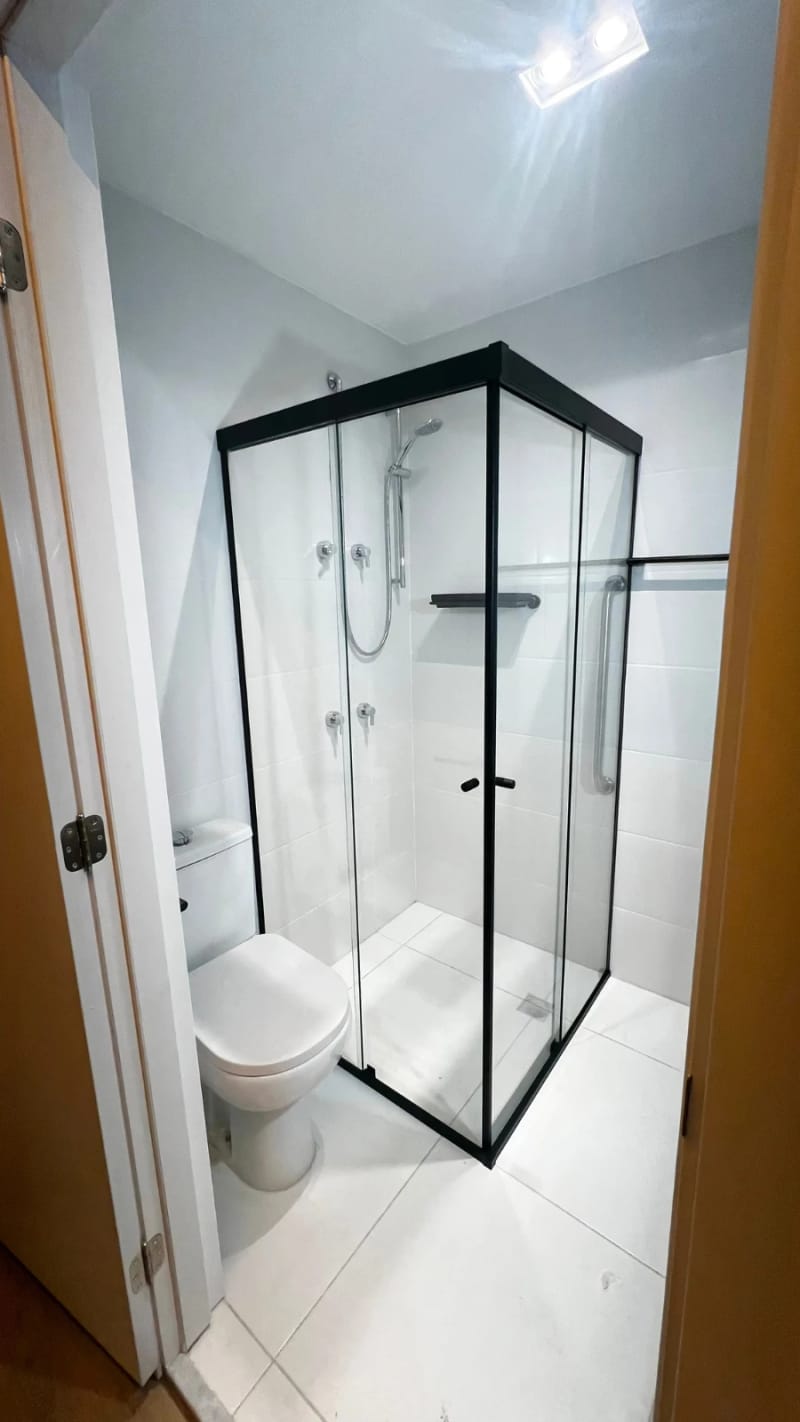 Box de canto em vidro incolor com perfil preto e puxador embutido, em banheiro branco de apartamento.