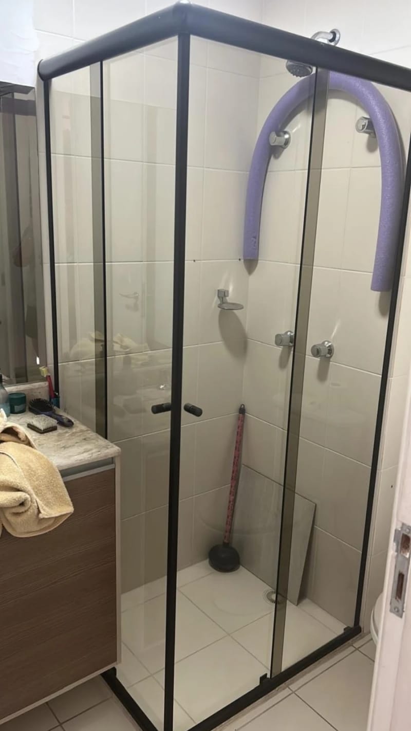 Box de canto em vidro incolor com perfil de alumínio preto e portas de correr, em banheiro de apartamento.