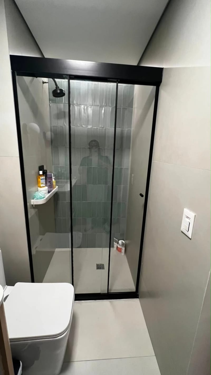 Box de correr em vidro incolor com perfil preto, em banheiro com revestimento ripado e nicho.