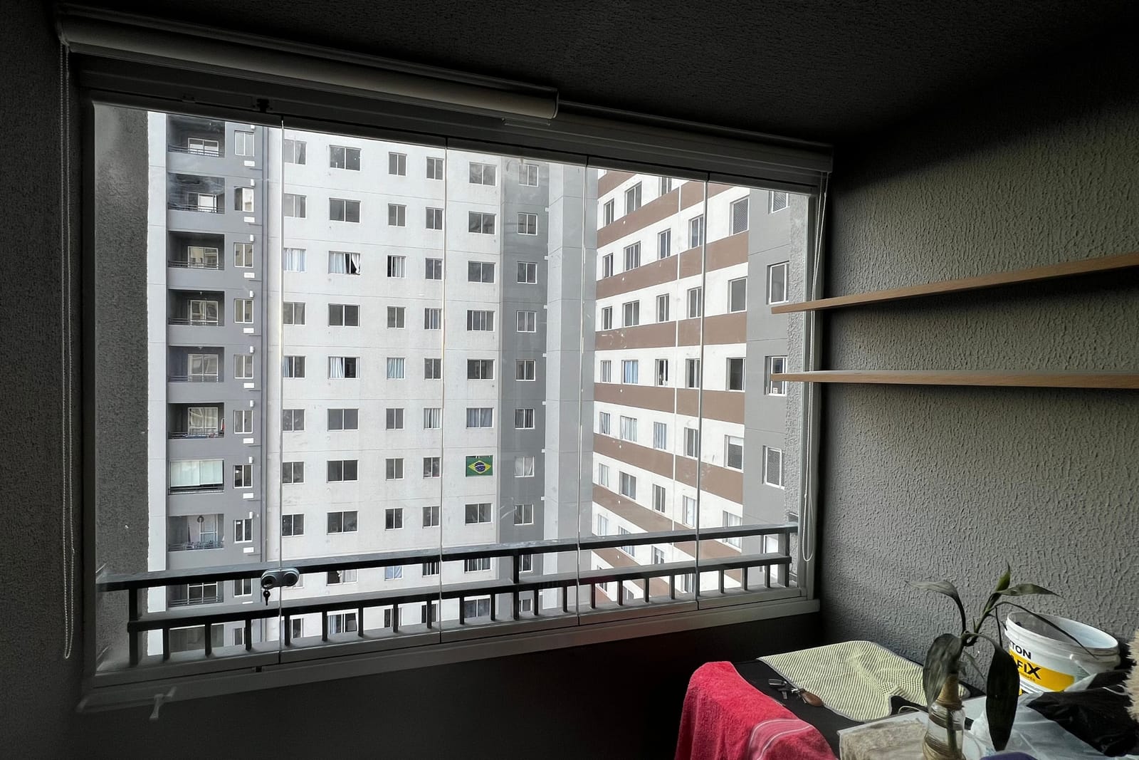 Sacada de apartamento fechada com vidro retrátil e esquadria escura, com vista para os prédios vizinhos. Obra da VitraAlu em Freguesia do Ó, São Paulo.