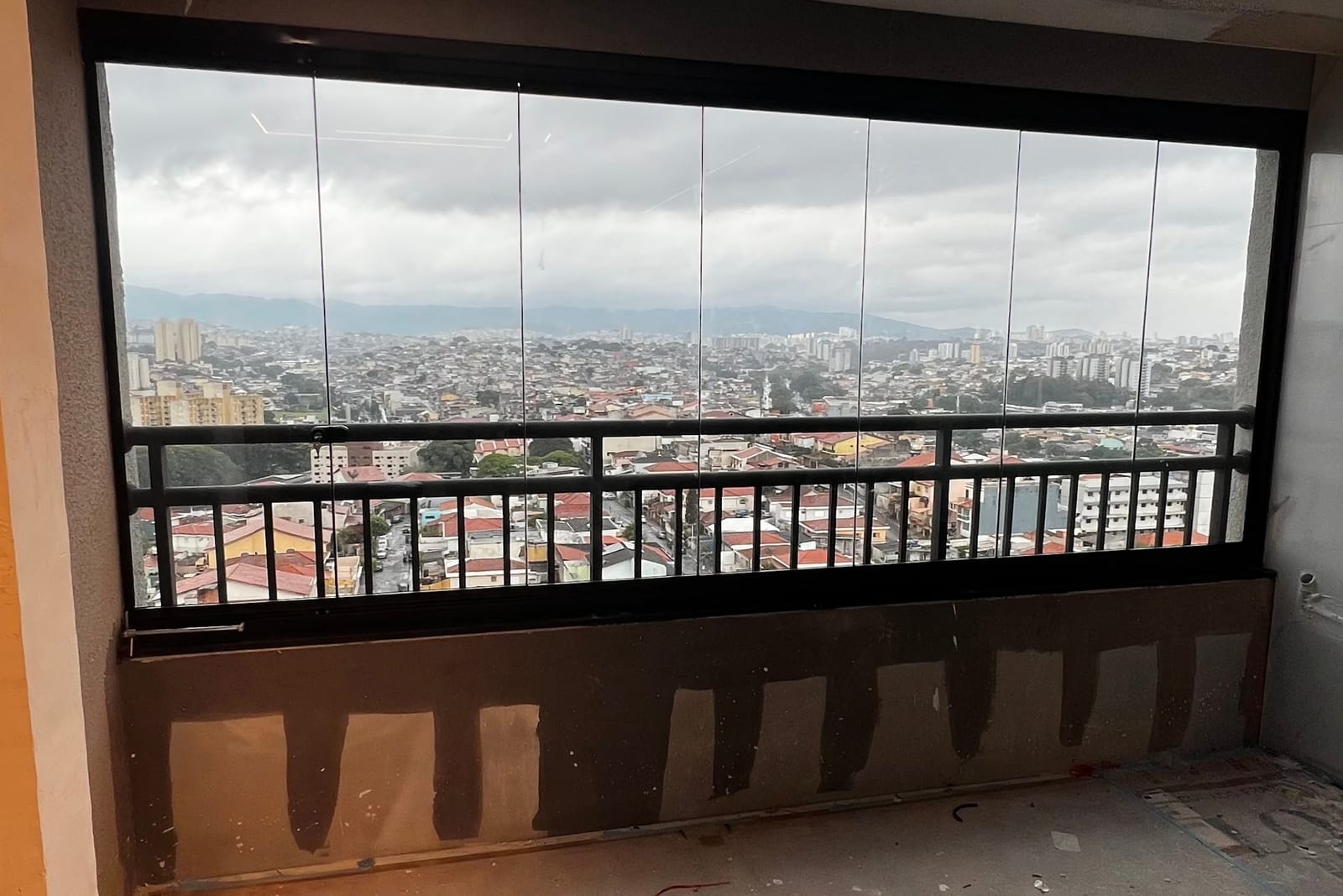 Varanda fechada com vidro e esquadria preta sobre anteparo, com vista panorâmica da cidade e da serra. Obra da VitraAlu em Freguesia do Ó, São Paulo.